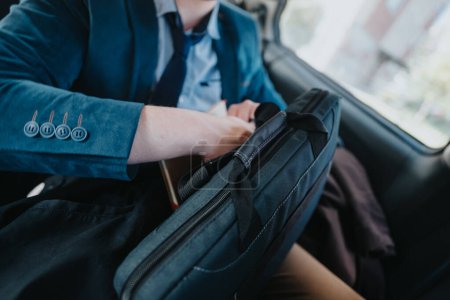 Un homme d'affaires bien habillé en costume bleu est vu ajuster les articles dans une mallette tout en étant assis dans une voiture, mettant l'accent sur la mobilité et la préparation.