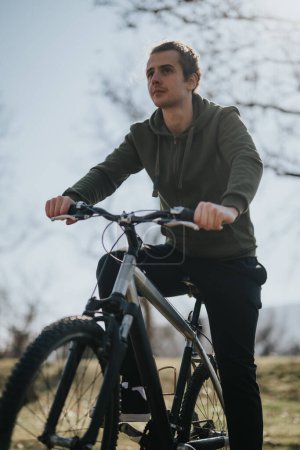Un joven adulto monta pensativamente su bicicleta en un parque, saboreando la tranquilidad y la belleza de un día soleado.