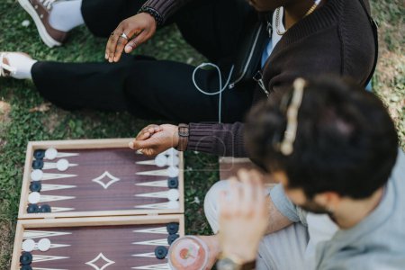Zwei Freunde unterschiedlicher Herkunft sitzen gemütlich im Freien und genießen ein unbeschwertes Backgammon-Spiel, die Wärme eines sonnigen Tages und die Freude an der Zweisamkeit..