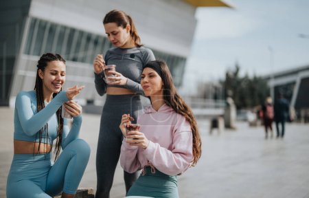 Drei Fitness-Enthusiasten, die nach einer Trainingseinheit eine Pause einlegen, um sich gesund zu ernähren und gemeinsam zu lachen und zu kleben.