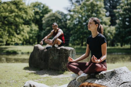 A young man and woman find tranquility while meditating on rocks in a lush urban park, depicting wellness and companionship.