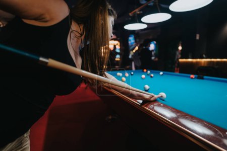 Focused young woman lining up her shot at a billiard game, surrounded by friends in a dynamic, well-lit pool hall.