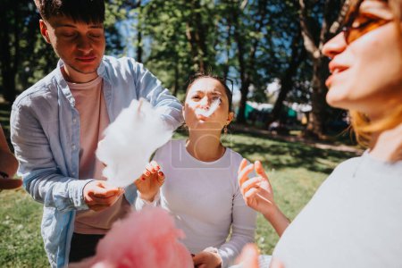 Un grupo de amigos disfrutan de un divertido día en el parque, riendo y compartiendo algodón de azúcar en un día soleado, capturando un momento de alegría y amistad.