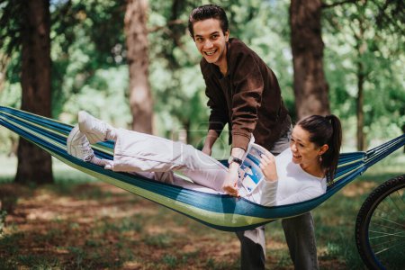 Un muchacho joven bromea juguetonamente a una muchacha absorta en un libro mientras que se relaja en una hamaca, capturando un momento de amistad alegre en un parque exuberante.