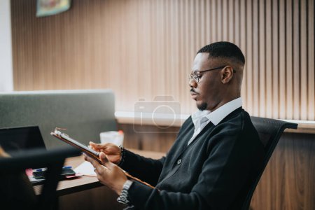 Empresario afroamericano profesional en un entorno de oficina moderno centrado en el trabajo mientras usa una tableta para analizar datos de negocios.