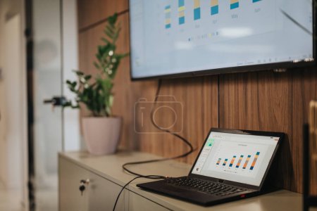 Une vue détaillée d'une salle de réunion d'affaires contemporaine avec des ordinateurs portables et un moniteur affichant des graphiques, présentant l'analyse des données et les résultats dans un environnement d'entreprise.