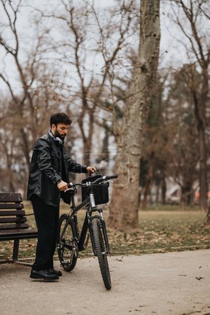 Un hombre de negocios guapo con un traje se para con su bicicleta en un parque de la ciudad, absorto en su trabajo en una computadora portátil.