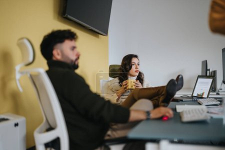Belle femme ayant une conversation avec son collègue masculin assis avec ses pieds sur le bureau de travail.