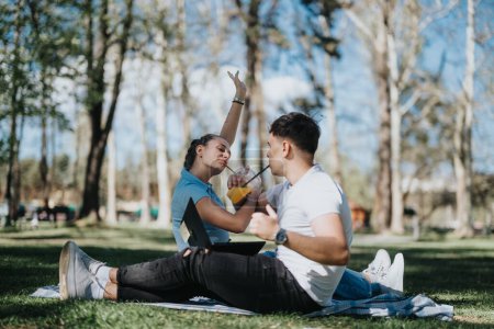Un hombre y una mujer jóvenes se sientan cara a cara en un parque soleado, compartiendo un momento de relajación y unión, rodeados de naturaleza.