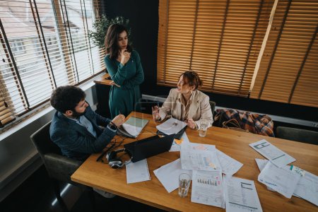 Tres profesionales de negocios examinan documentos y participan en una discusión en una mesa de madera en un entorno de oficina contemporáneo.