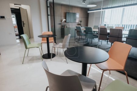 Ein zeitgenössisches Büro mit einer Vielzahl bunter Stühle an kleinen Tischen, minimalistisch und stilvoll gestaltet, geeignet für Besprechungen oder Gelegenheitsarbeiten.