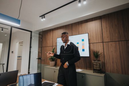 Jeune homme d'affaires confiant donnant une présentation sur la croissance financière en utilisant des graphiques colorés dans une salle de réunion de bureau bien équipée et contemporaine.