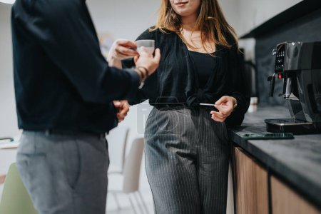 Two coworkers in a modern office kitchen, sharing a pleasant conversation with coffee cups in hand during a workday break.
