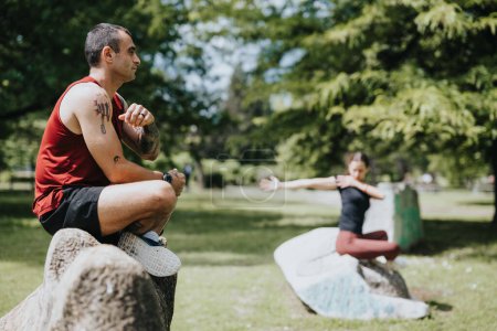 Un hombre y una amiga participan en ejercicios de yoga en un exuberante parque verde, demostrando concentración y trabajo en equipo.