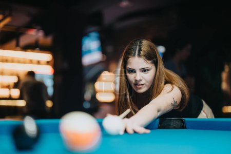 Eine fokussierte junge Frau spielt Billard und bereitet sich darauf vor, in einer belebten Bar einen Schuss abzugeben. Sie verkörpert Muße und Präzision im Spiel.