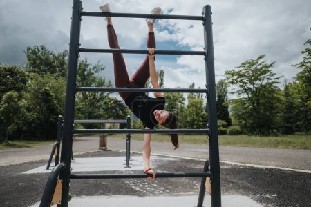 Lebendige Aufnahme einer jungen athletischen Frau, die in einem Park einen umgekehrten Hang an Fitness-Bars praktiziert und dabei Stärke und Beweglichkeit demonstriert.