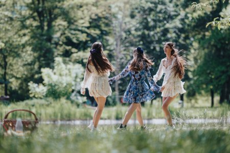 Trois jeunes filles, peut-être s?urs, partagent un moment joyeux dansant sans soucis dans un parc verdoyant par une journée ensoleillée du printemps, incarnant la liberté.