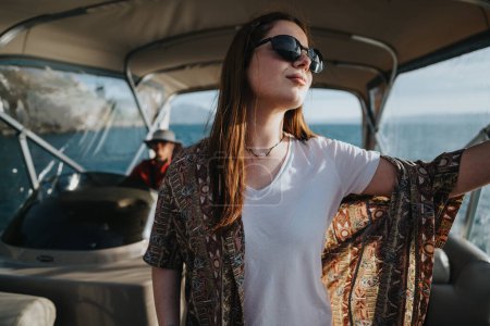 Eine fröhliche Frau mit Sonnenbrille breitet ihre Arme auf einem Boot aus und spürt die Freiheit, während ein Freund navigiert, was einen perfekten Urlaubstag auf dem See widerspiegelt..