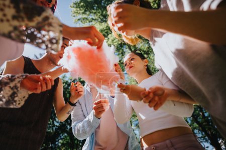 A group of young adult friends enjoy a sunny day in the park, sharing pink candy cotton, embodying joy and freedom.