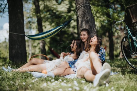 Drei Schwestern entspannen und lachen gemeinsam an einem sonnigen Tag im Park, genießen die Natur und die Gesellschaft in der Nähe einer Hängematte und eines Fahrrads.