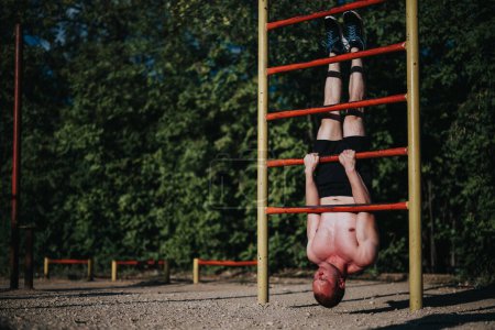 Homme effectuant un exercice intense de la tête sur l'équipement de gymnastique en plein air dans un parc, mettant en valeur la force et l'équilibre
