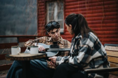 Zwei junge Erwachsene unterhalten sich im Freien, bei einer Gitarre und Kaffee auf einem Tisch an einer Holzkabine.