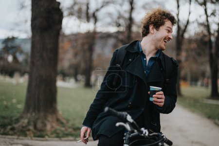 A happy curly-haired young man enjoys a leisurely walk in the park with a cup of coffee, exuding casual style and positivity.