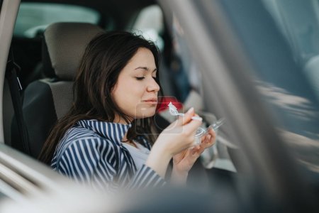 Eine junge Frau sitzt in ihrem Auto und lächelt sanft, während sie in einer Pause einen gesunden Snack aus einem Plastikbehälter genießt..