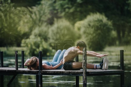 Couple engaged in a synchronized exercise routine on a wooden bridge amidst beautiful natural surroundings by the lake. Serene outdoor fitness and wellness activity.