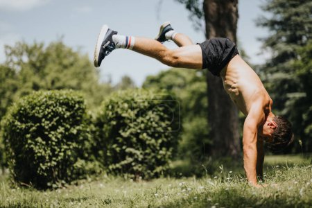 Athletic young man performing a handstand outdoors in a park on a sunny day, showcasing strength, fitness, and balance.