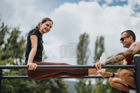 Un homme et une femme se livrent à des exercices d'étirement dans un parc de conditionnement physique extérieur, démontrant leur travail d'équipe et leur forme physique sous un ciel dégagé..