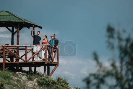 Grupo de amigos tomando una selfie en un mirador de madera en la naturaleza, disfrutando del aire libre y capturando recuerdos juntos.
