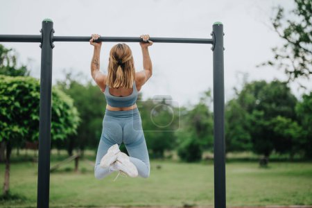 Woman doing pull ups in a park, focusing on exercising biceps and shoulders. A healthy, active lifestyle showcased in an outdoor setting.