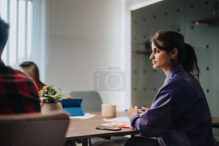 A professional businesswoman attentively listens and participates in a strategic meeting with coworkers in a contemporary designed office space.