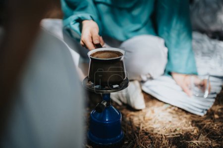 Nahaufnahme einer Person, die Kaffee auf einem tragbaren Herd im Wald aufbrüht, um ein Outdoor-Campingerlebnis und Entspannung festzuhalten.