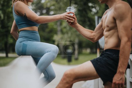 Young athletic couple sharing a drink after an outdoor workout in the park. Healthy lifestyle and fitness concept.