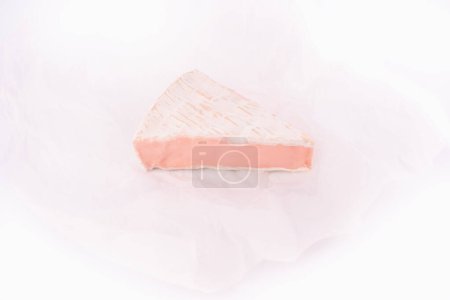 Foto de A piece of french soft cheese on the white baker paper. Image isolated on a white background - Imagen libre de derechos