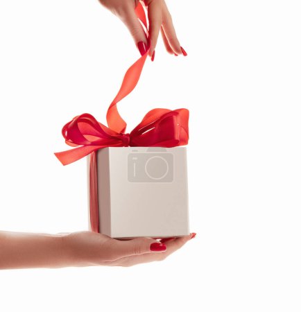 Foto de La mano de una hermosa mujer tirando de un lazo rojo desenvolviendo una caja de regalo blanca - Imagen libre de derechos