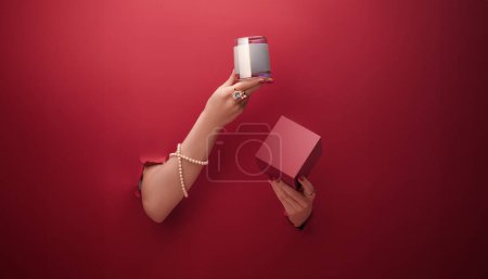 Téléchargez les photos : Les mains sortent d'un fond rouge et tiennent une bougie avec une boîte, un concept d'affiche publicitaire ou une bannière - en image libre de droit