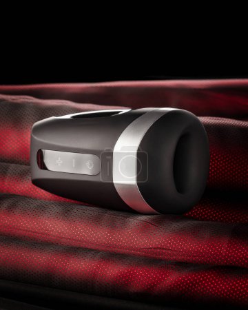 Modern black luxurious male masturbator with warming function presented on red mesh textured fabric, designed for unforgettable sensual climaxes for men. Concept of sex toys for adult pleasur