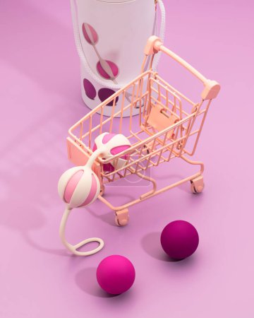 Téléchargez les photos : Boules vaginales vibrantes en silicone placées dans un mini chariot sur fond rose. Concept ludique de shopping intime féminin moderne. Sex toys pour adultes - en image libre de droit