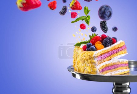 Téléchargez les photos : Superbe gâteau aux fruits en couches avec des flocons d'amandes garnis de baies fraîches en vol dynamique sur fond de dégradé bleu serein, symbolisant fraîcheur et saveur. Confiserie art traditions concept - en image libre de droit