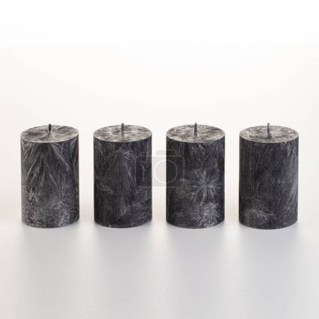 Foto de Conjunto de cuatro velas de cera de palma negra con patrones únicos similares al hielo dispuestos sobre fondo blanco. Concepto de accesorios artesanales elegantes que añaden un toque moderno a la decoración del hogar o de la oficina - Imagen libre de derechos
