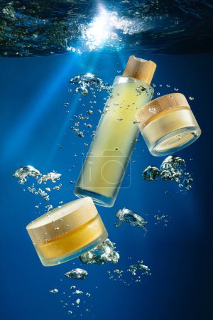 Bottles of skincare products with wooden caps, lighted by sun rays penetrating deep blue ocean depths, floating surrounded by air bubbles. Concept of natural skin care, deep nourishment and hydration