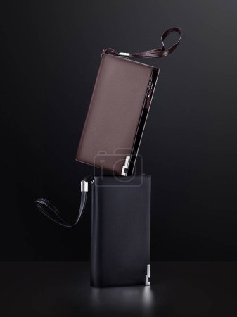 Zwei strapazierfähige, bequeme Ledergeldbörsen in schwarz und braun mit Reißverschluss und dekorativen silbernen Metalldetails vor dunklem Hintergrund. Anspruchsvolle und praktische Accessoires für Männer