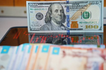 Foto de Almaty, Kazajstán - 10.04.2022: Gráficos de existencias en la tableta y tenge y billetes de dólar sobre la mesa. - Imagen libre de derechos