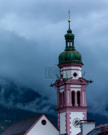 Foto de Austria, Tirol, Innsbruck, campanario de la iglesia Servitenkirche en el fondo de la montaña en las nubes - Imagen libre de derechos