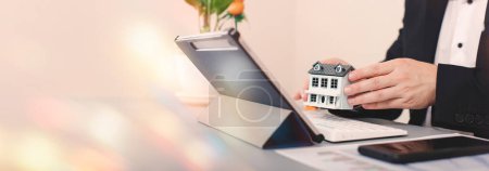 Photo for Real estate agent holding house model in front of laptop. Real estate business - Royalty Free Image