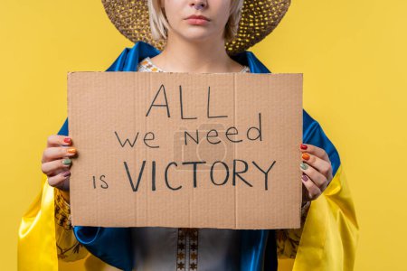 Foto de Mujer ucraniana con cartón Todo lo que necesitamos es victoria sobre fondo amarillo. Ucrania ganará la guerra. Democracia, libertad, manifestación, concepto de agresión rusa. Alta calidad - Imagen libre de derechos