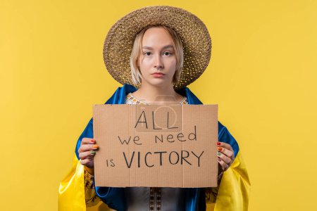 Foto de Mujer ucraniana con cartón Todo lo que necesitamos es victoria sobre fondo amarillo. Ucrania ganará la guerra. Democracia, libertad, manifestación, concepto de agresión rusa. Alta calidad - Imagen libre de derechos